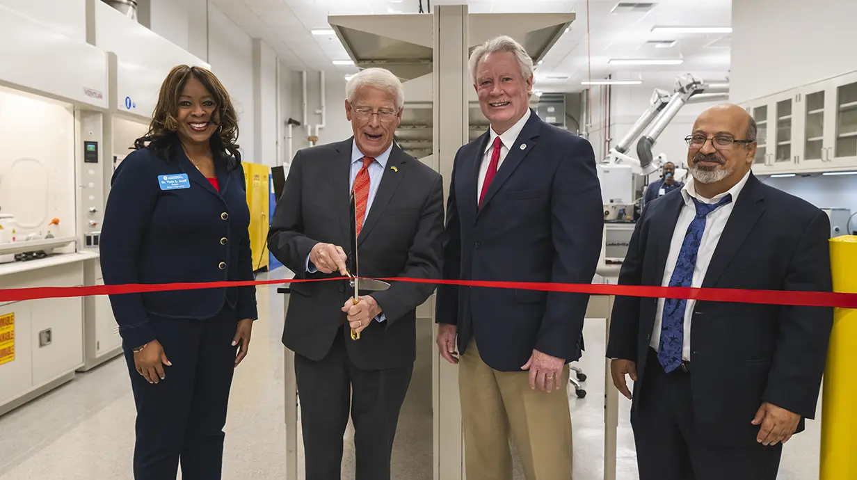 A woman and three men cut a ribbon at a research facility.